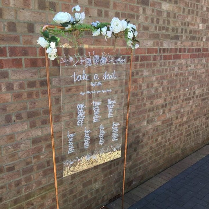 Clear Acrylic Table Plan hanging from copper pipe frame with flowers