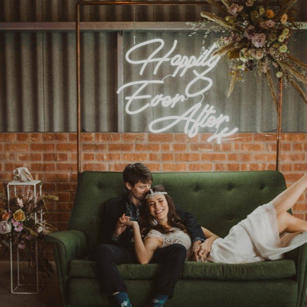 bride and groom on couch in front of happily ever after neon sign